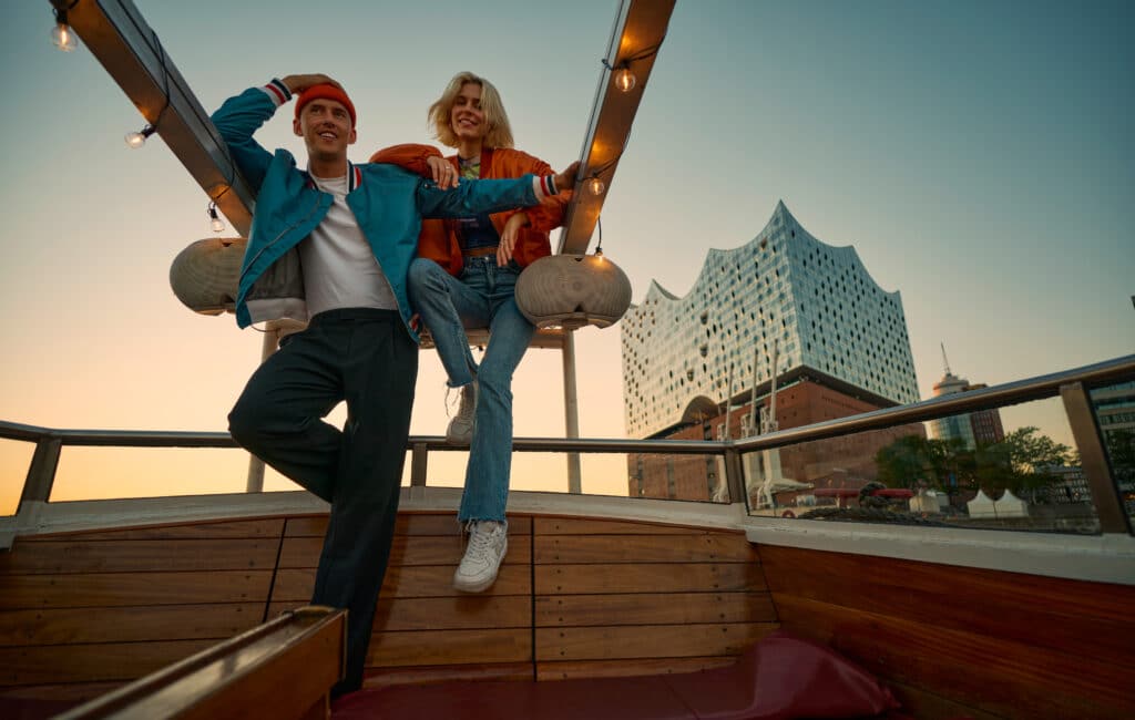 Foto von zwei jungen Menschen, die auf einem Schiff an der Elbphilharmonie vorbeifahren.