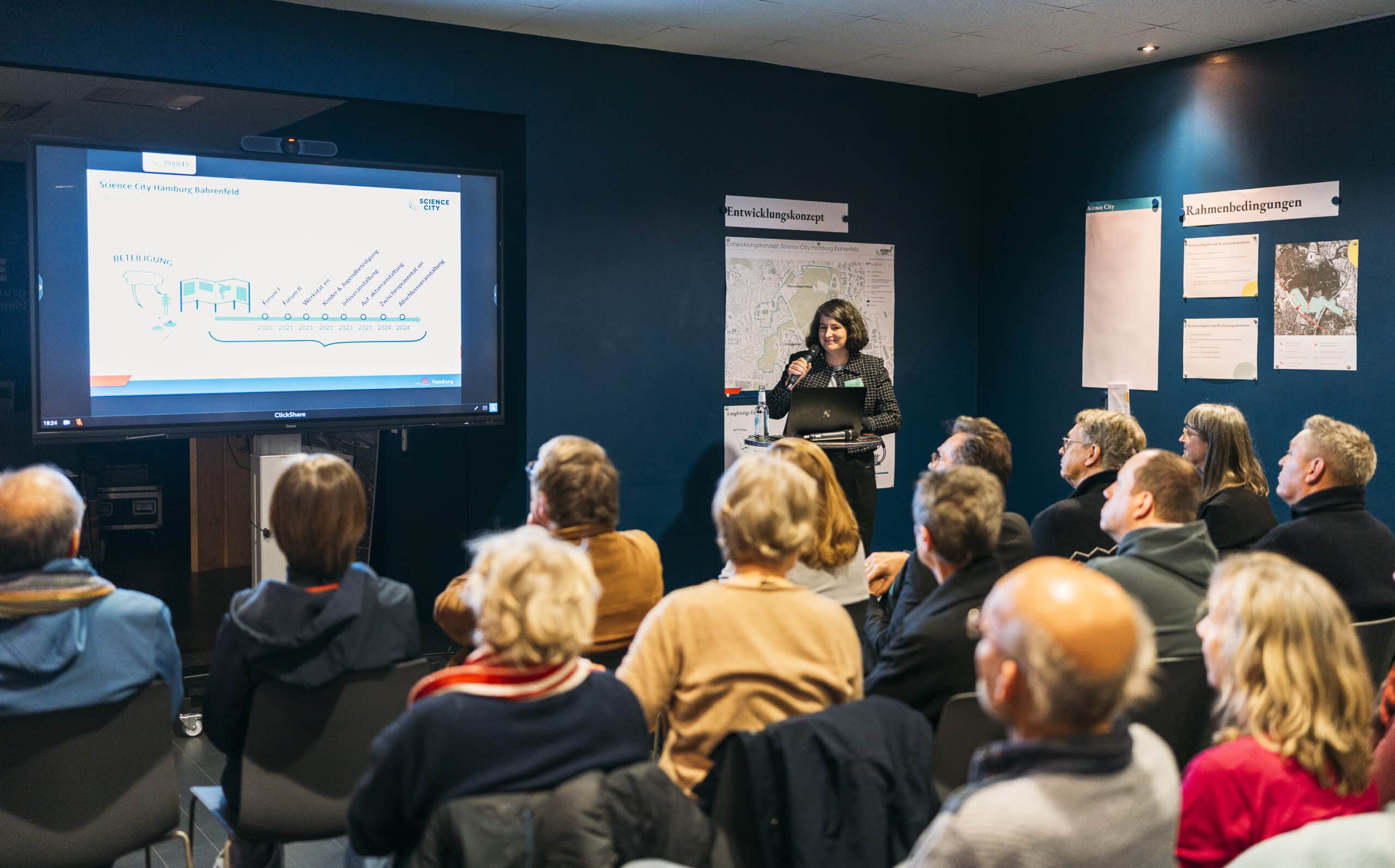 Mehrere Personen schauen sich im Rahmen einer Infoveranstaltung die Präsentation zum Entwicklungskonzept der Science City Hamburg Bahrenfeld an.