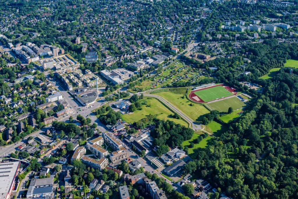 Luftaufnahme eines Stadtteils, der von großen Grünflächen dominiert wird. Am rechten Bildrand befindet sich ein Fußballplatz.